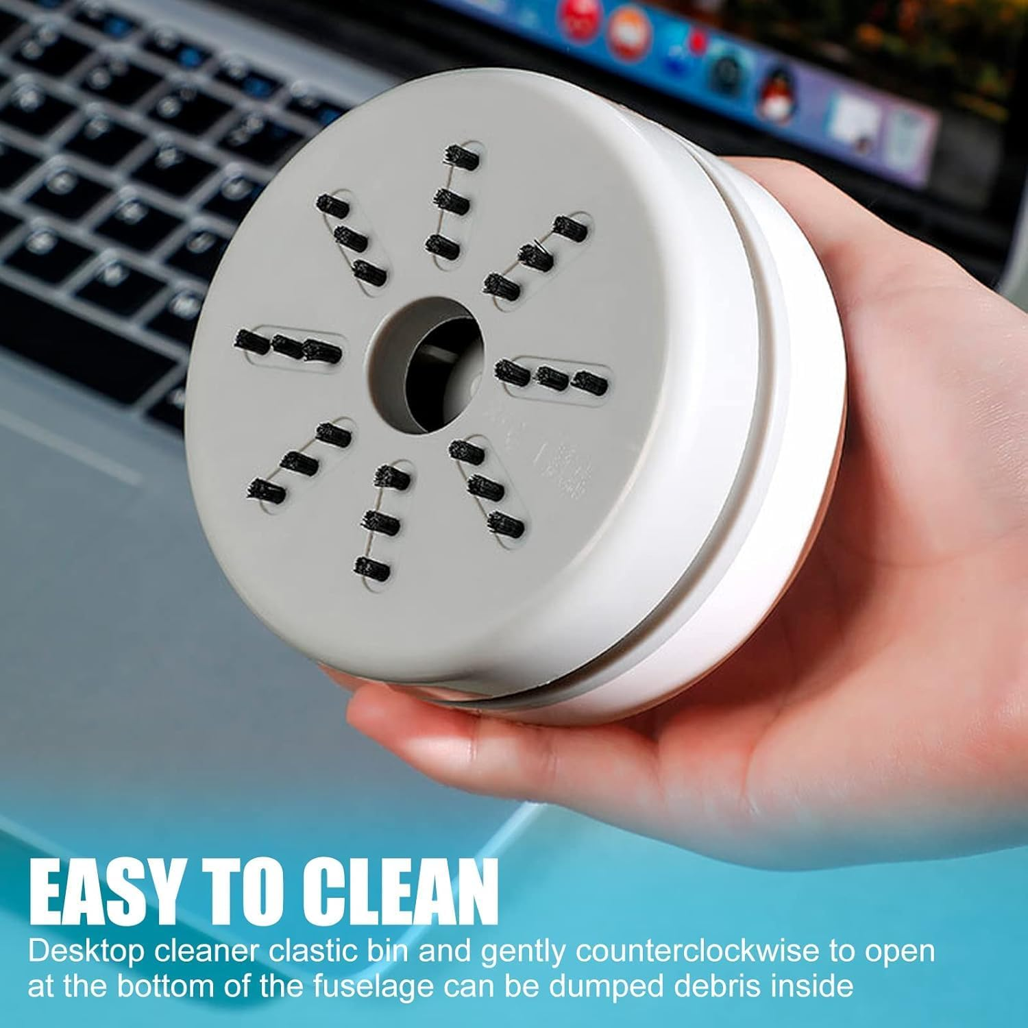Eine Hand hält einen weißen Desktop-Staubsauger mit Bürsten vor einer Tastatur.