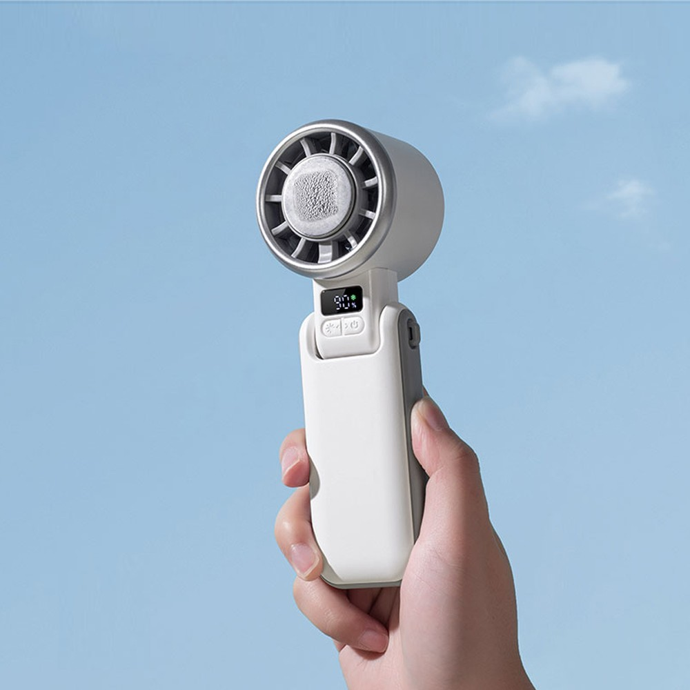 Una mano sostiene un ventilador portátil blanco con borde plateado contra un cielo azul.