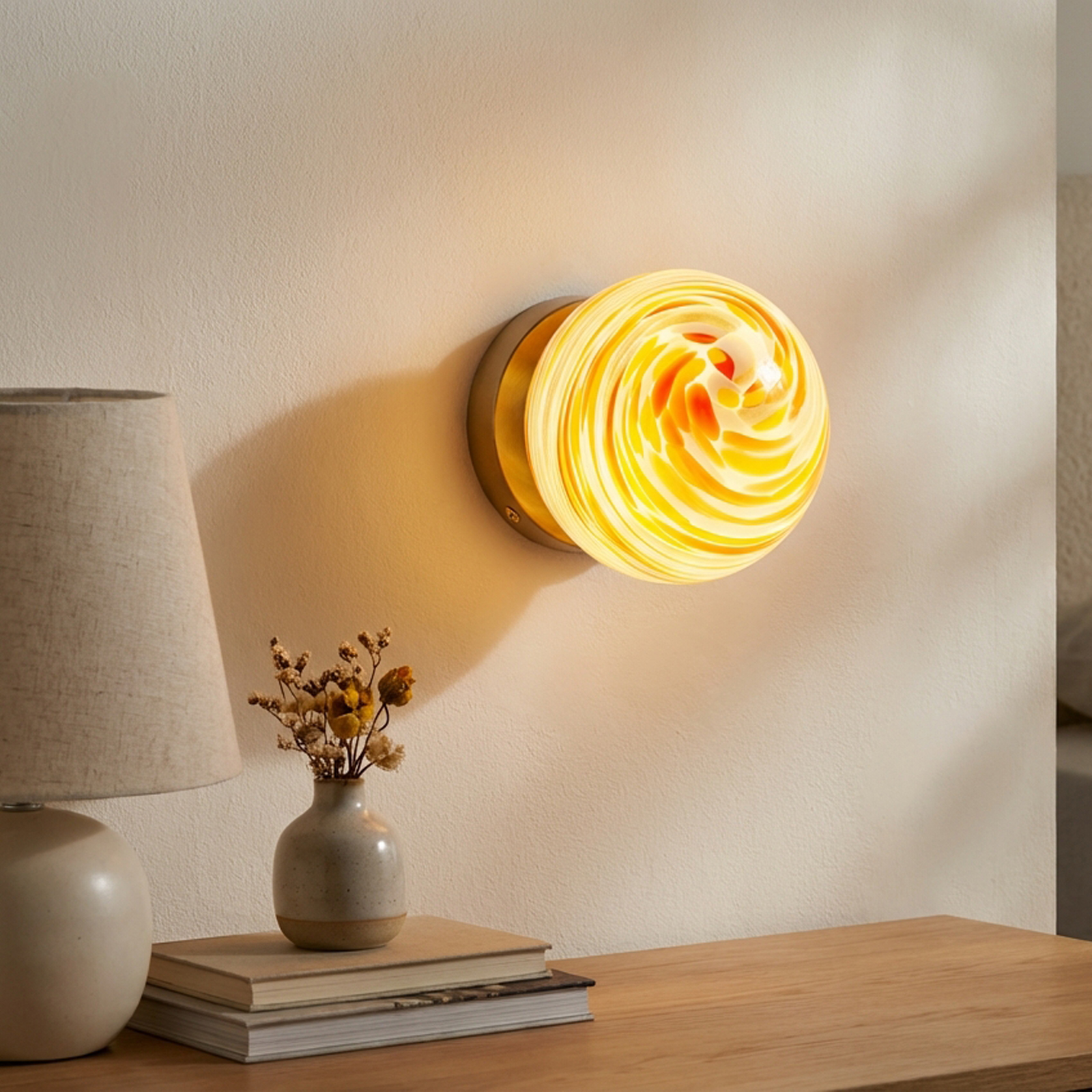 Una lámpara de pared con cristal de remolino amarillo y naranja cuelga en una pared color crema.