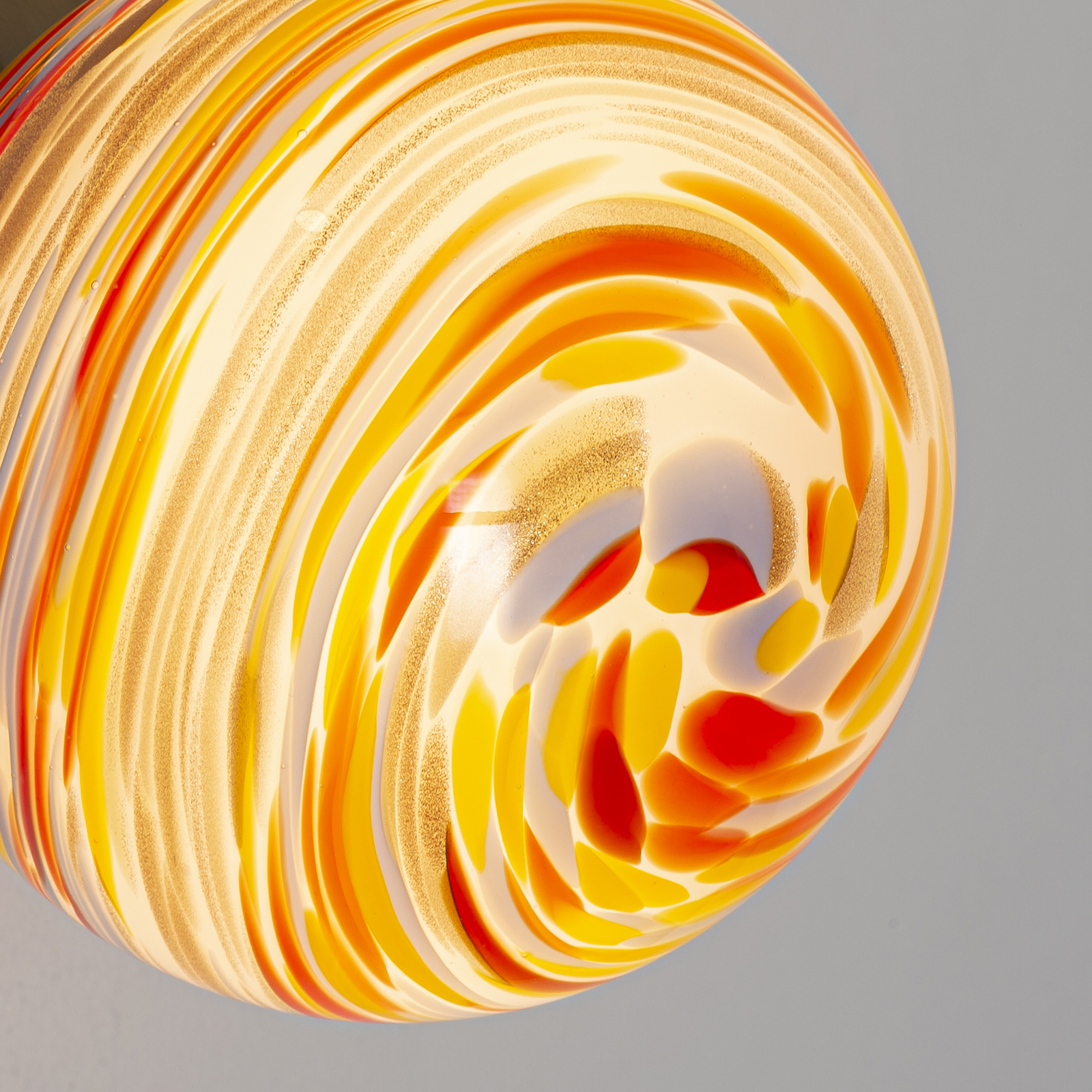 Una lámpara de vidrio colorida con patrones en espiral en naranja, amarillo y rojo sobre fondo claro.