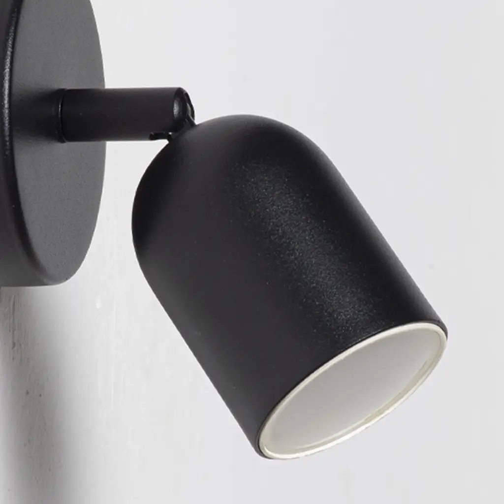 Un foco de pared negro y ajustable con interior blanco, montado en una pared blanca.