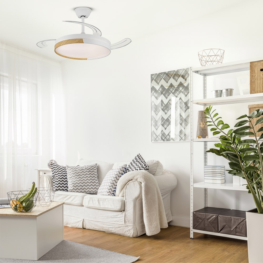 Un ventilador de techo blanco con detalle de madera sobre un sofá blanco con cojines.