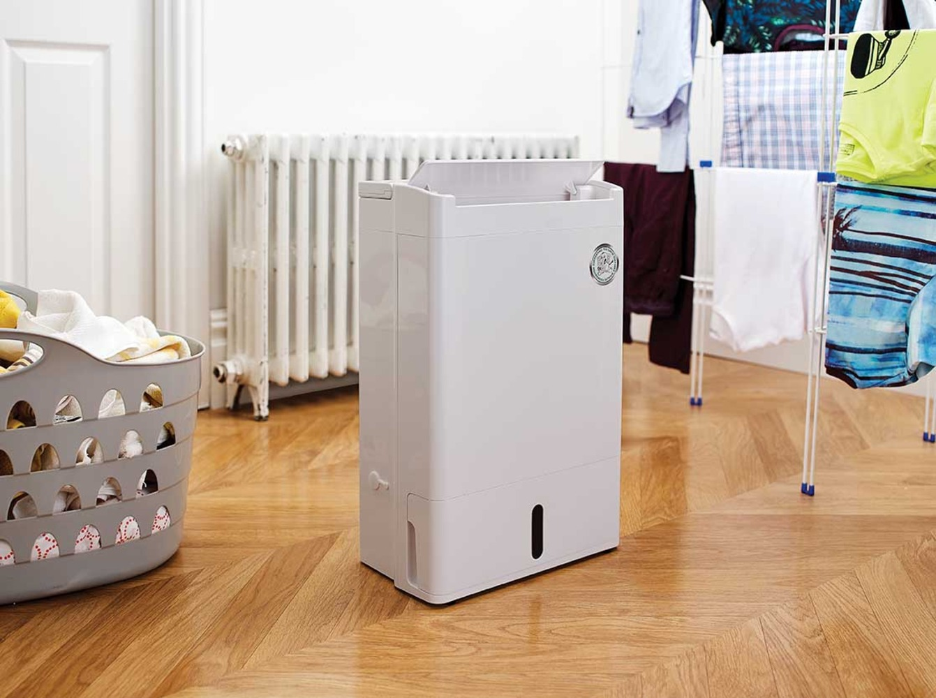A white dehumidifier stands next to a drying rack with clothes.