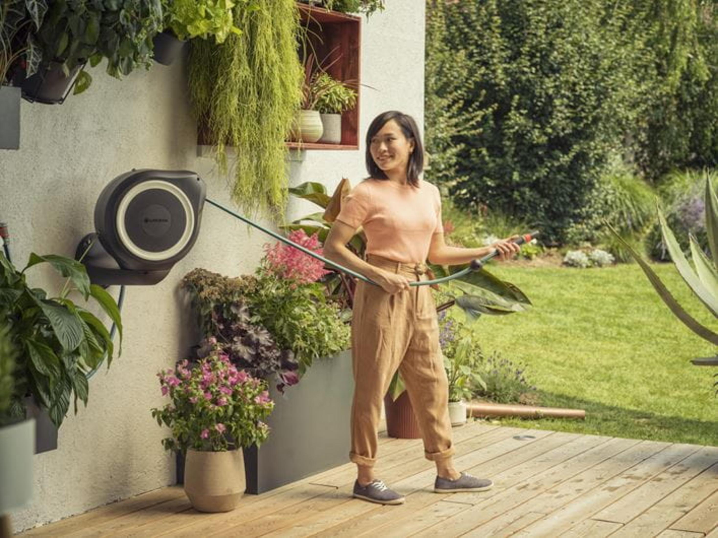 Una donna anna le piante con un tubo in un giardino lussureggiante.