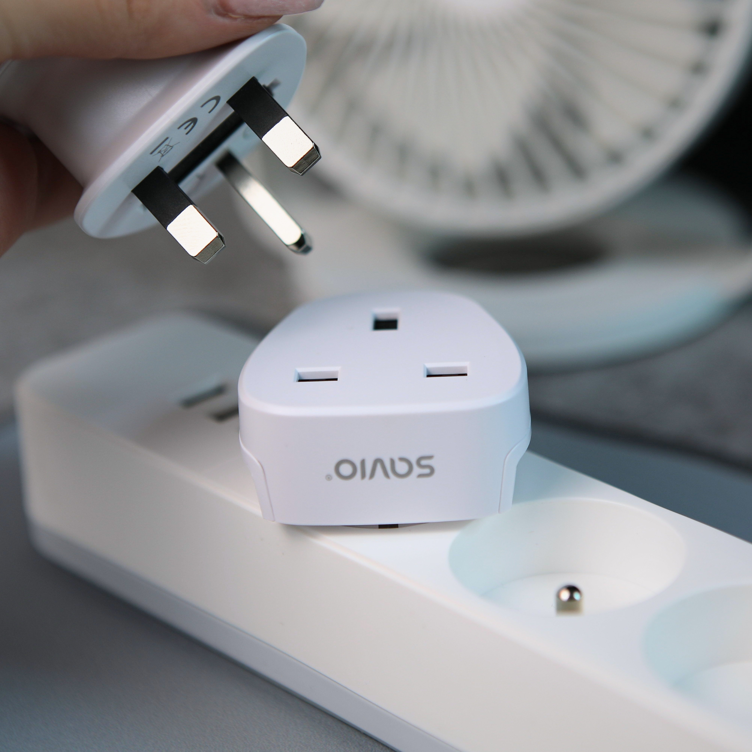 Dłoń trzyma białą wtyczkę brytyjską nad białym przedłużaczem z białym adapterem.