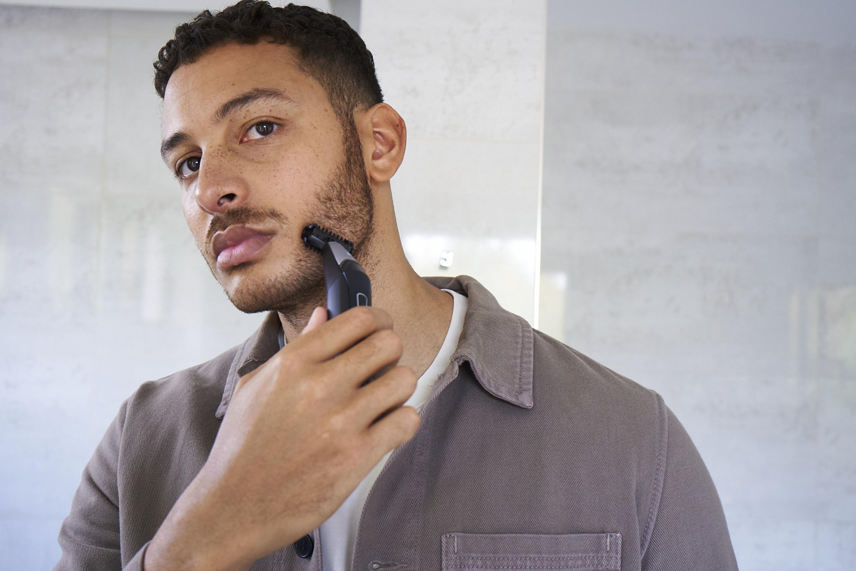Mężczyzna z ciemnymi włosami przycina brodę czarną maszynką.