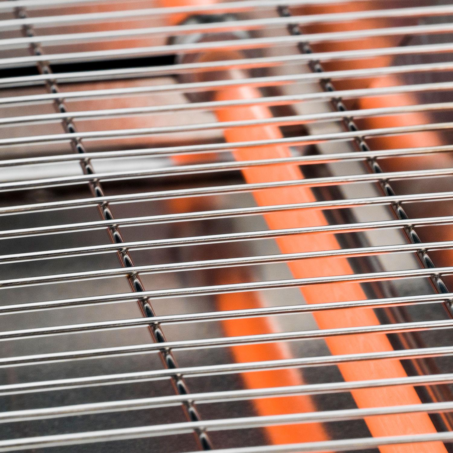 Close-up van een metalen grillrooster met oranje achtergrond.
