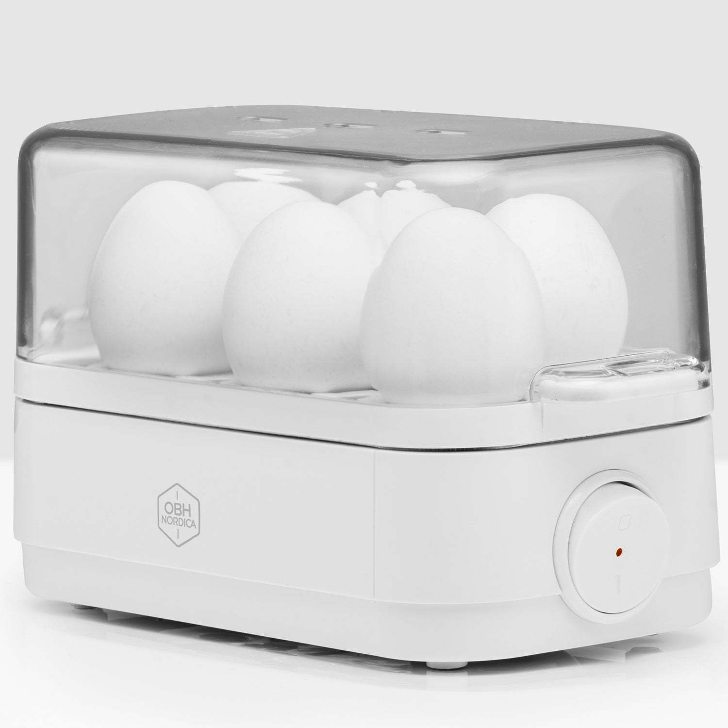 White egg cooker with clear lid holding six white eggs. OBH Nordica logo visible.