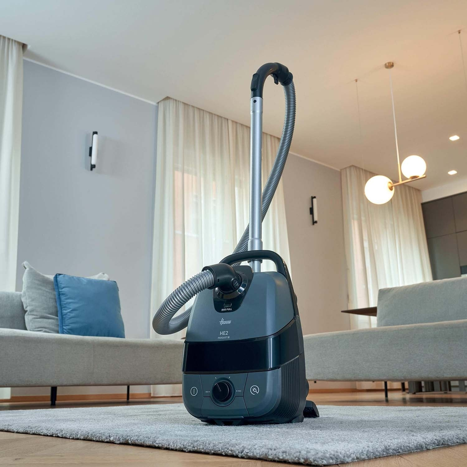 Een grijze stofzuiger staat op een kleed in een moderne woonkamer.