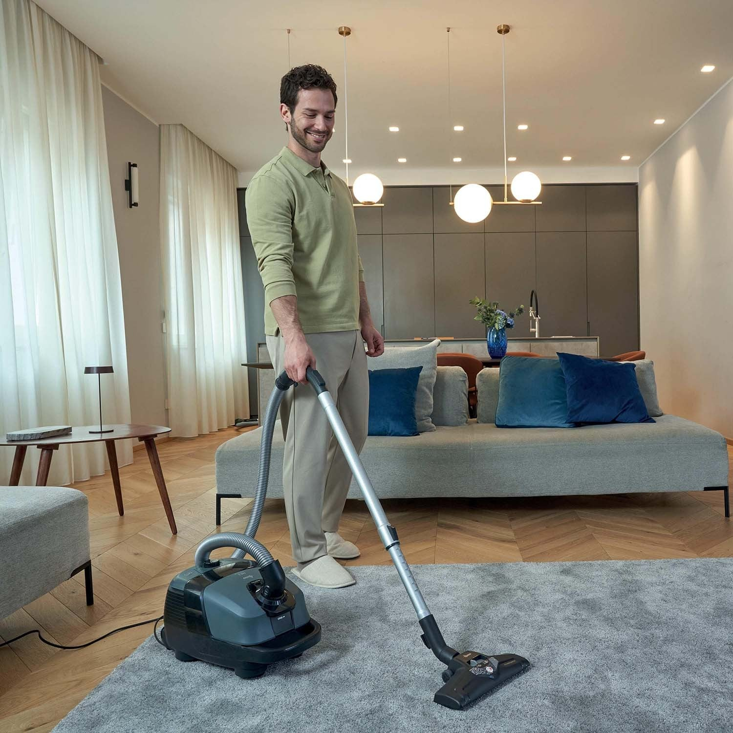 Man stofzuigt grijze vloer in moderne woonkamer met bank.