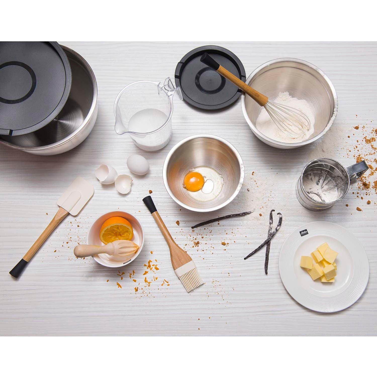 Bak ingrediënten en gereedschap: kommen, eieren, bloem, boter, sinaasappel, garde, spatel, kwast, vanille.