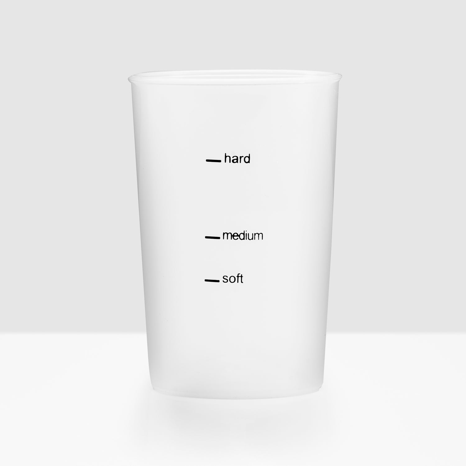 A white cup with markings for hard, medium, and soft.