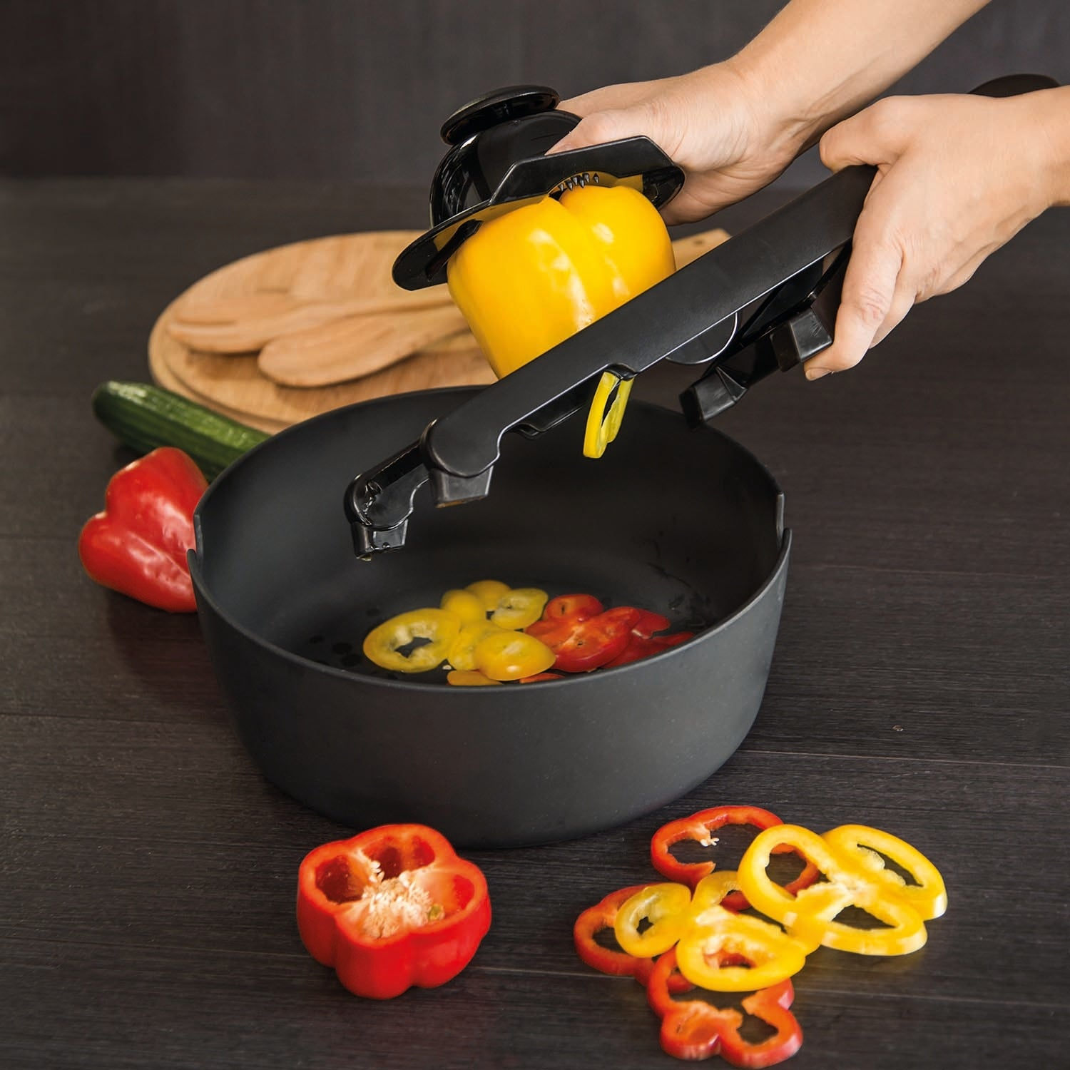 Handen snijden gele paprika in plakjes boven een kom met paprikaplakjes. Rode peper, komkommer.