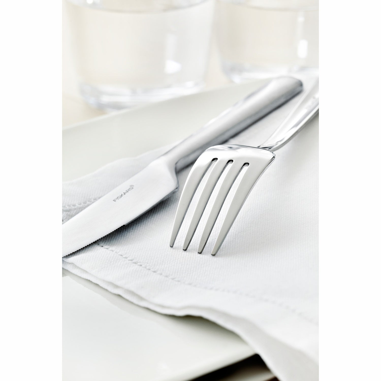 A fork and knife rest on a white napkin, with glasses in the background.
