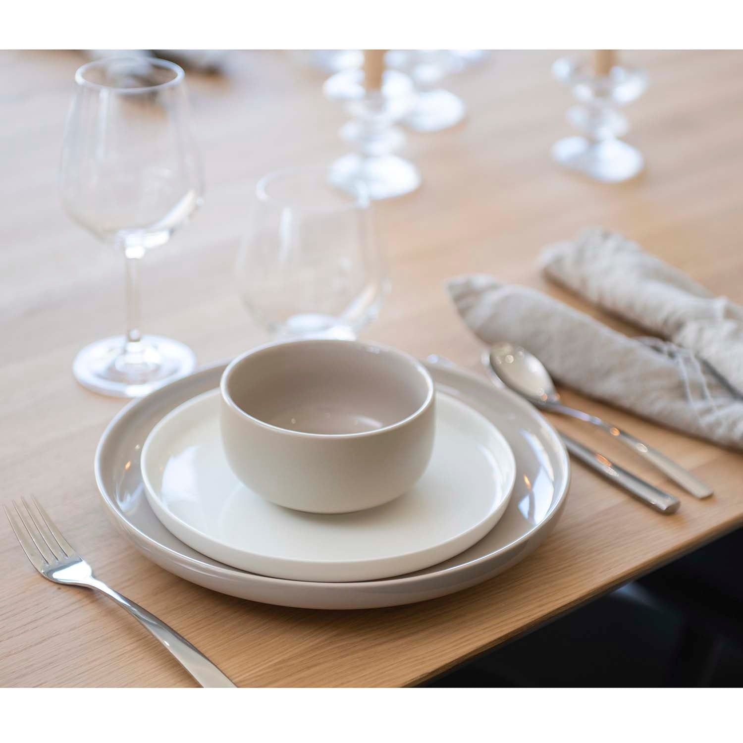 A set table with plates, bowl, cutlery, glasses, and cloth napkins.