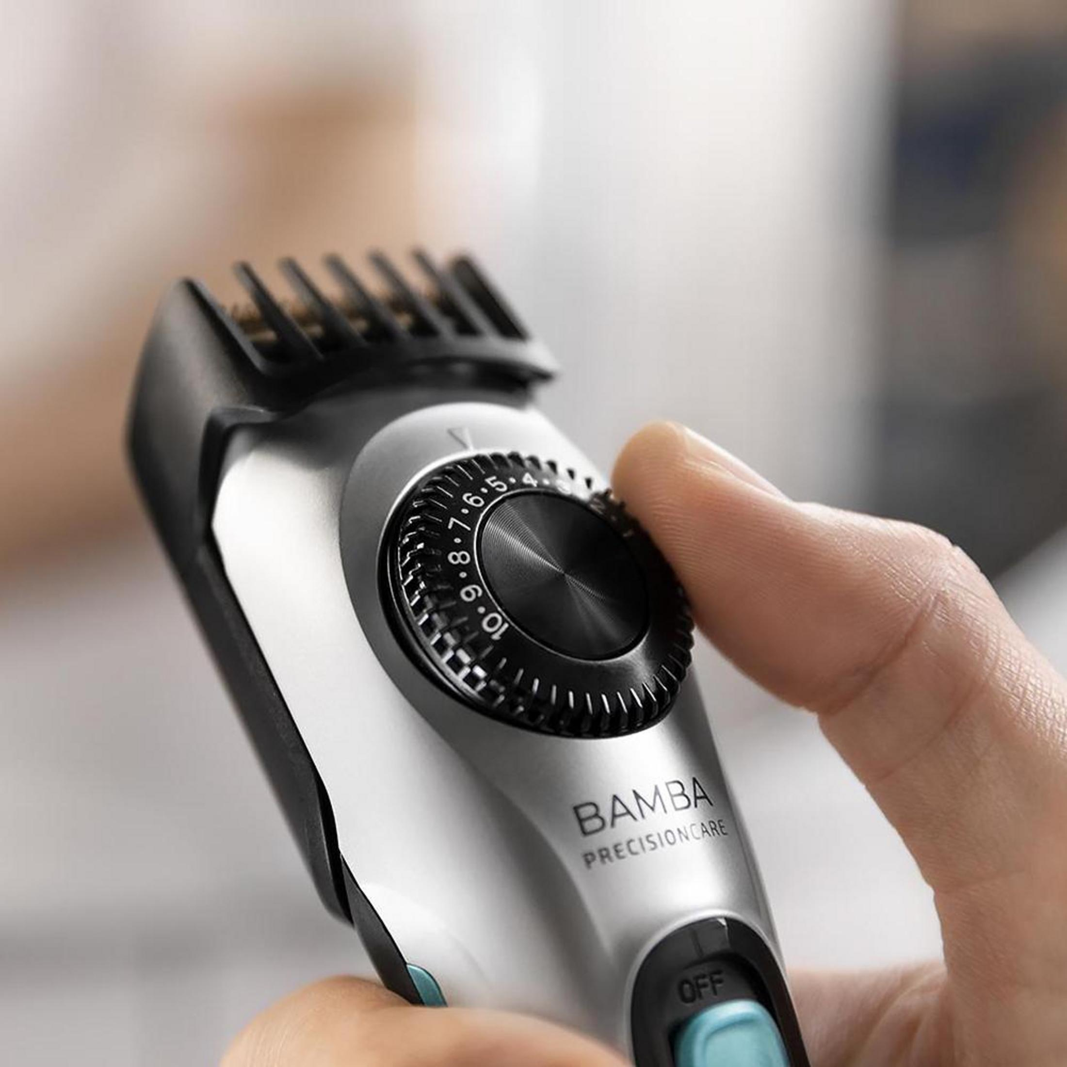 Een hand houdt een zilveren haartrimmer vast met een zwarte instelknop.