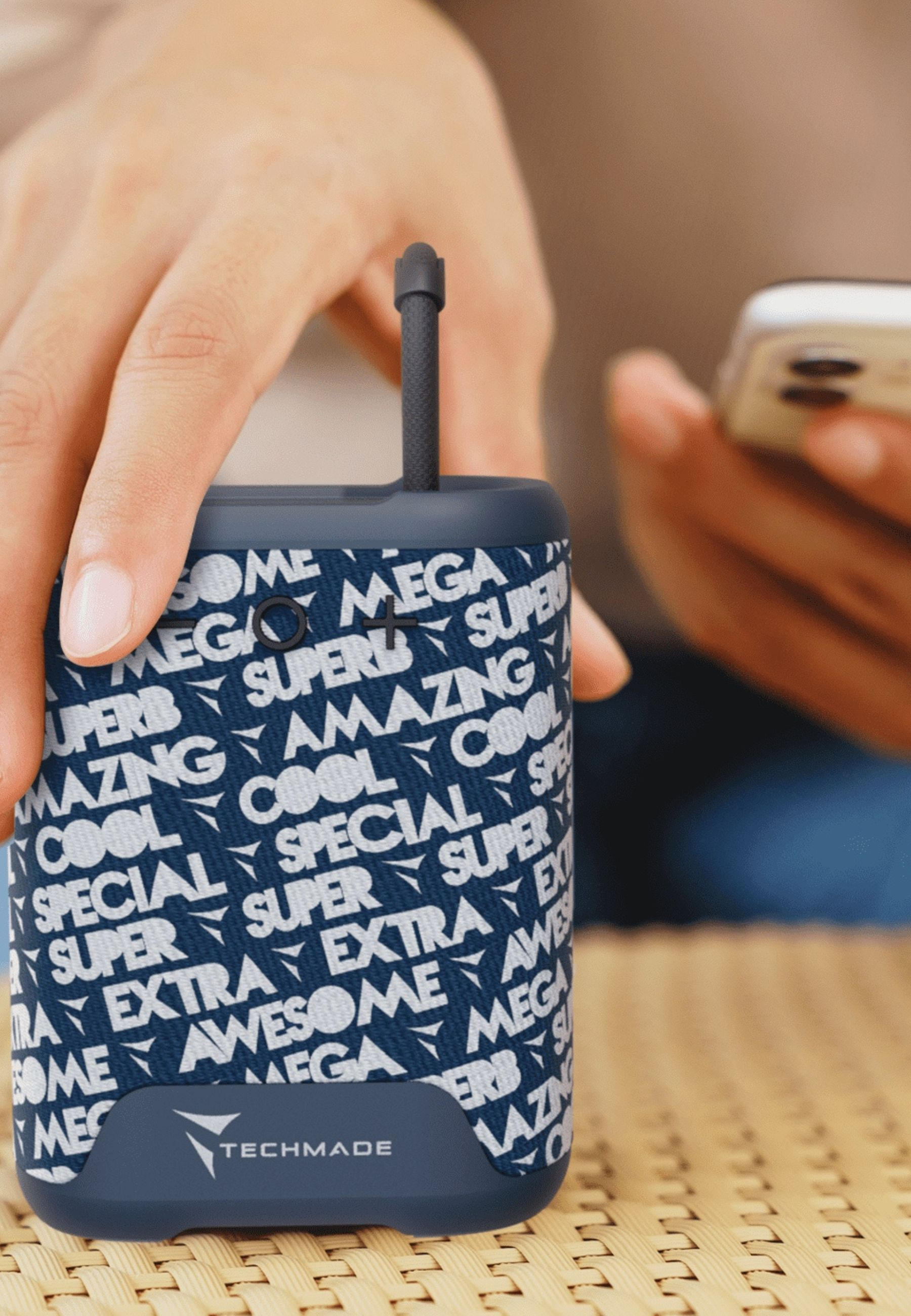 Una mano tiene un power bank blu scuro con motivo testuale bianco. Una persona usa un cellulare.
