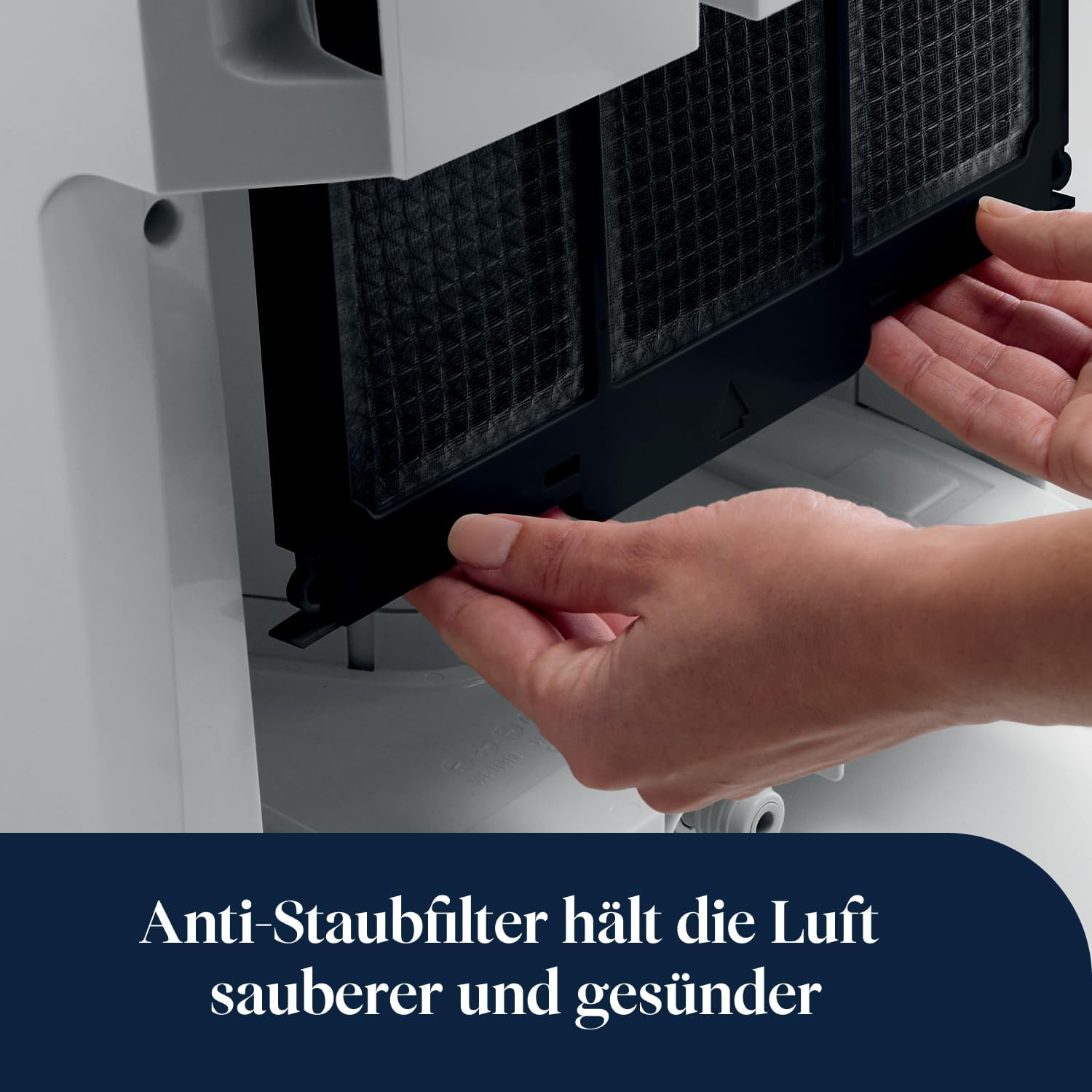 Ręce wyjmują czarny filtr przeciwkurzowy z białego urządzenia.