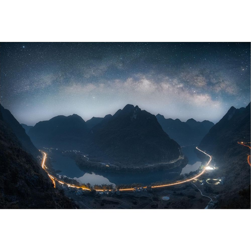 Montagne sotto il cielo stellato con strada e fiume illuminati.