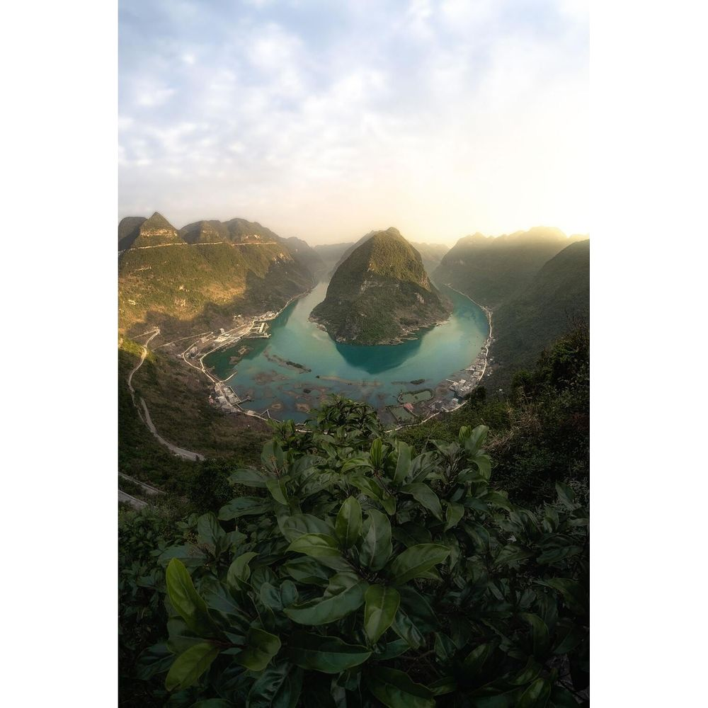 Un fiume serpeggia tra montagne verdi con un'isola al centro.
