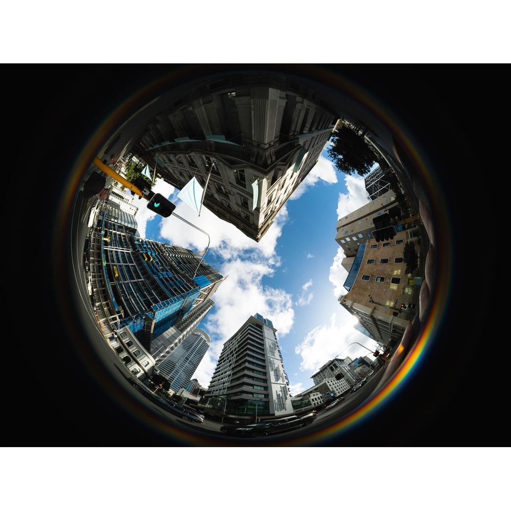 Fisheye view of buildings and sky with rainbow light effect.