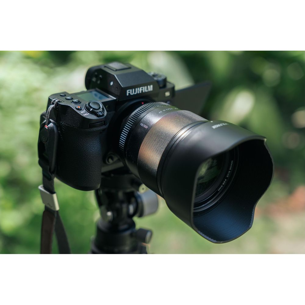Una fotocamera Fujifilm nera con obiettivo su treppiede, sfondo verde sfocato.