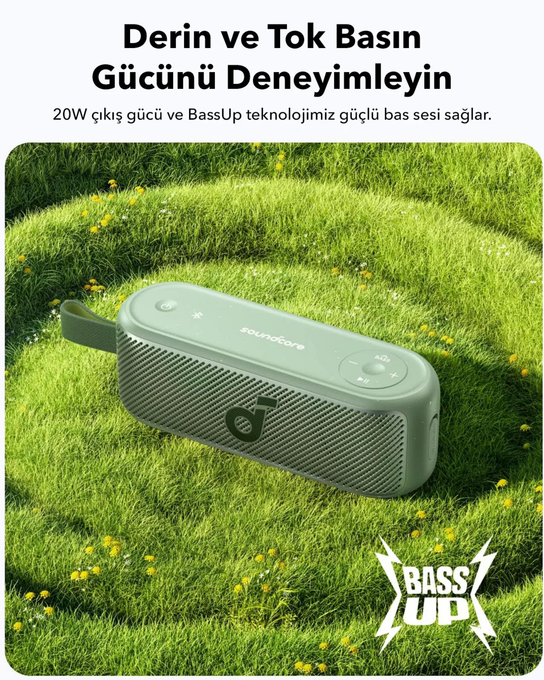 Un altoparlante Soundcore verde su erba verde con fiori gialli.