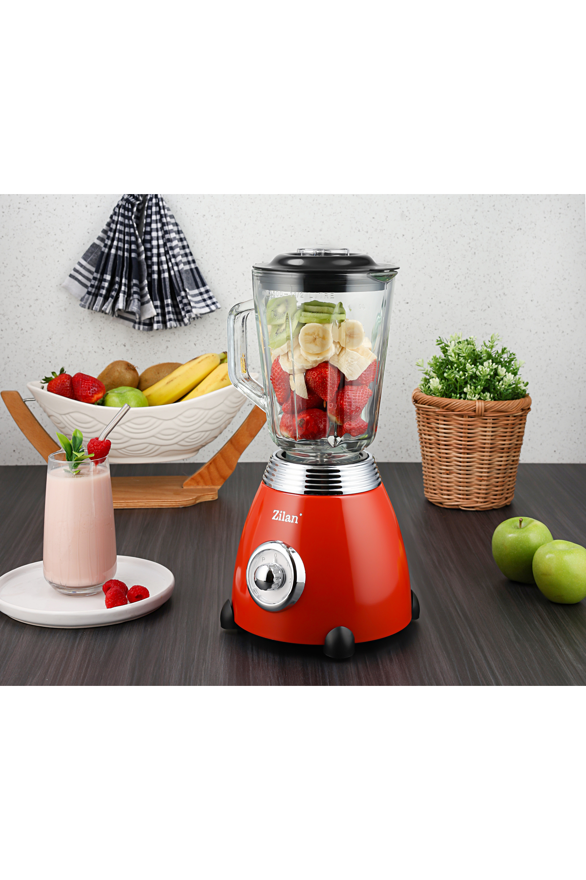 Meyve dolu kırmızı blender, yanında bir bardak smoothie ve elmalar.