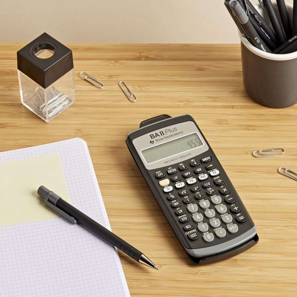 Calculatrice, pot à crayons avec trombones, carnet et stylo sur bureau bois.