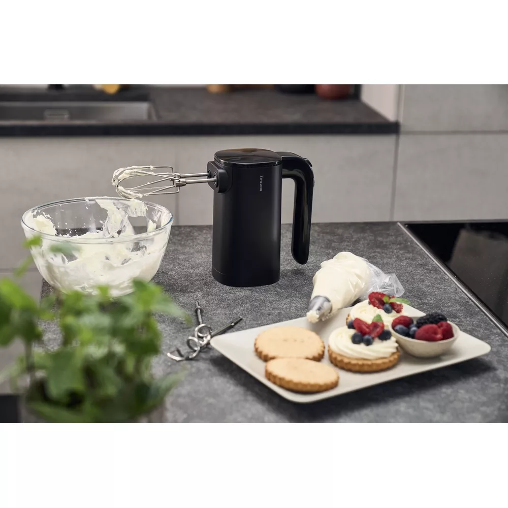 Schwarzer Handmixer neben Schüssel mit Sahne und fertigen Torten.