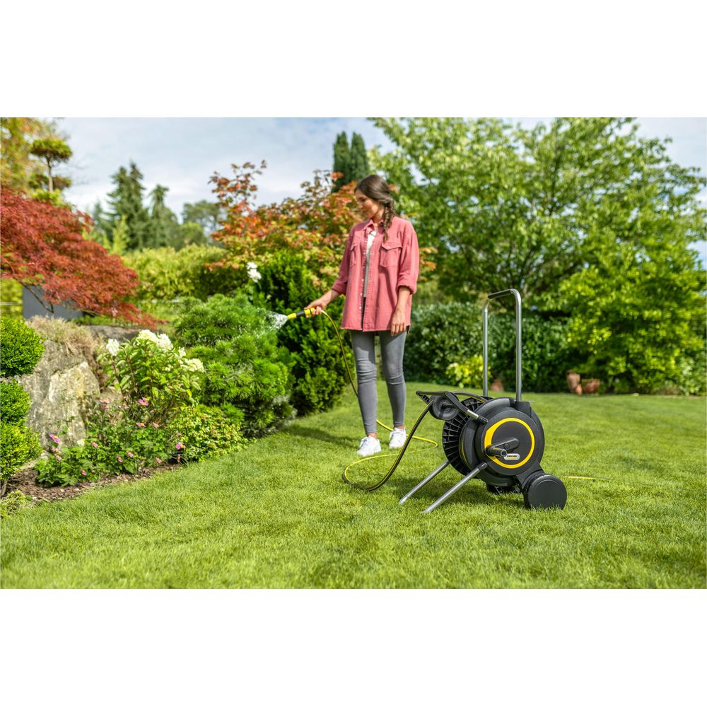 Frau wässert Büsche im Garten mit einem Schlauch neben einem Schlauchwagen.