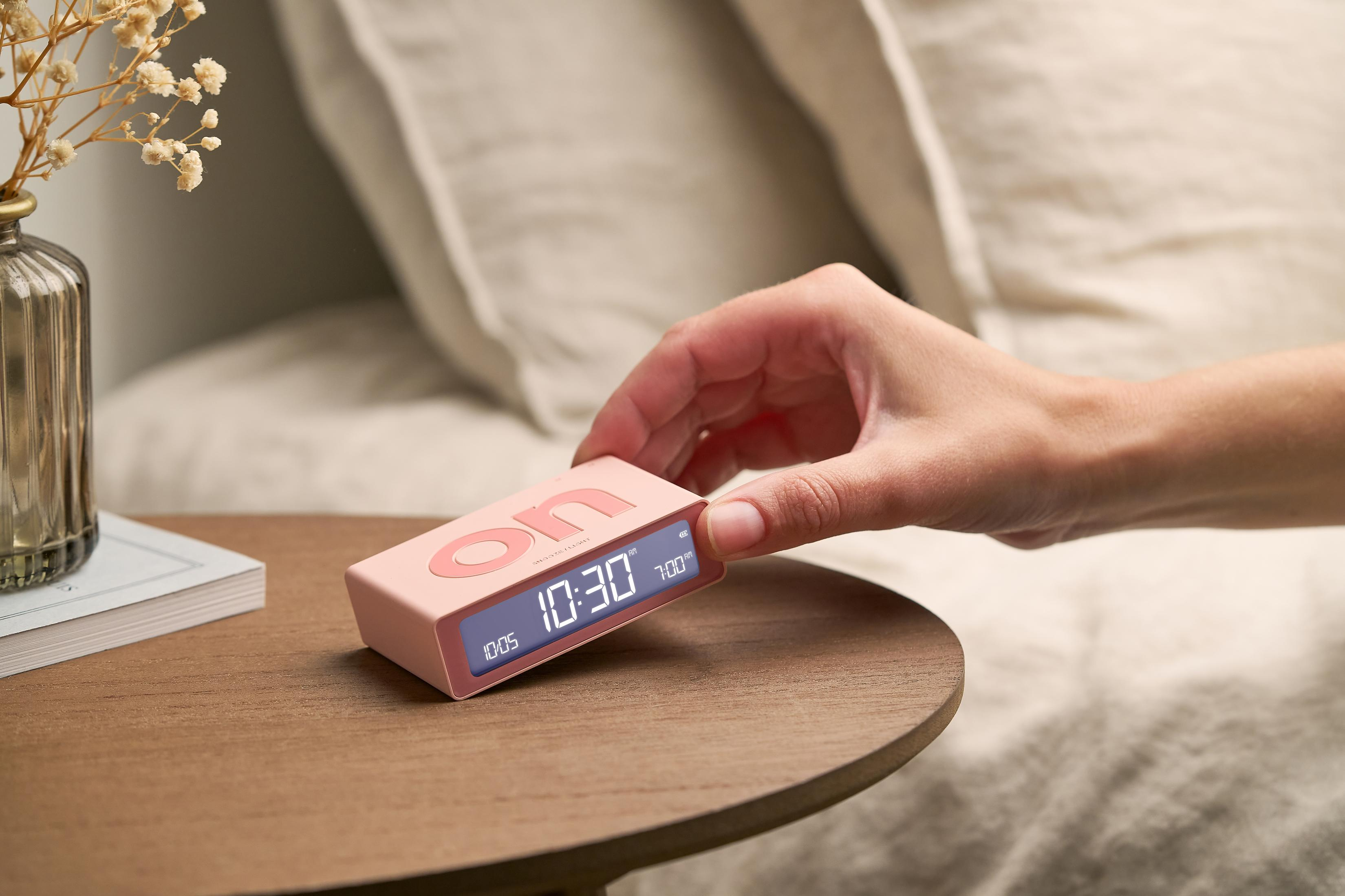 Hand stellt rosafarbenen Wecker mit digitaler Anzeige 10:30 auf Tisch.