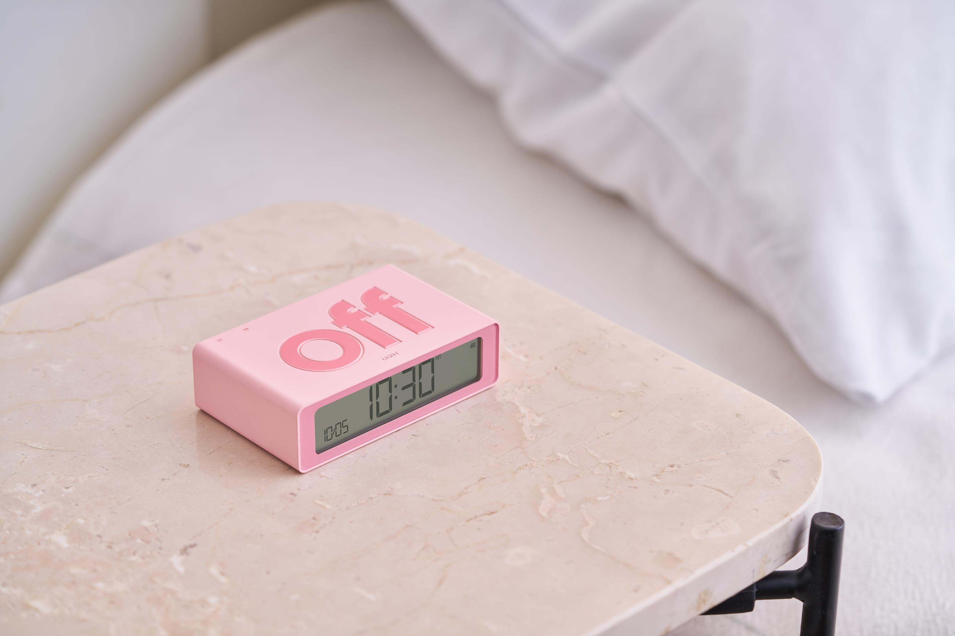 Ein rosa Wecker mit der Aufschrift "off" auf einem Marmortisch neben einem Bett.
