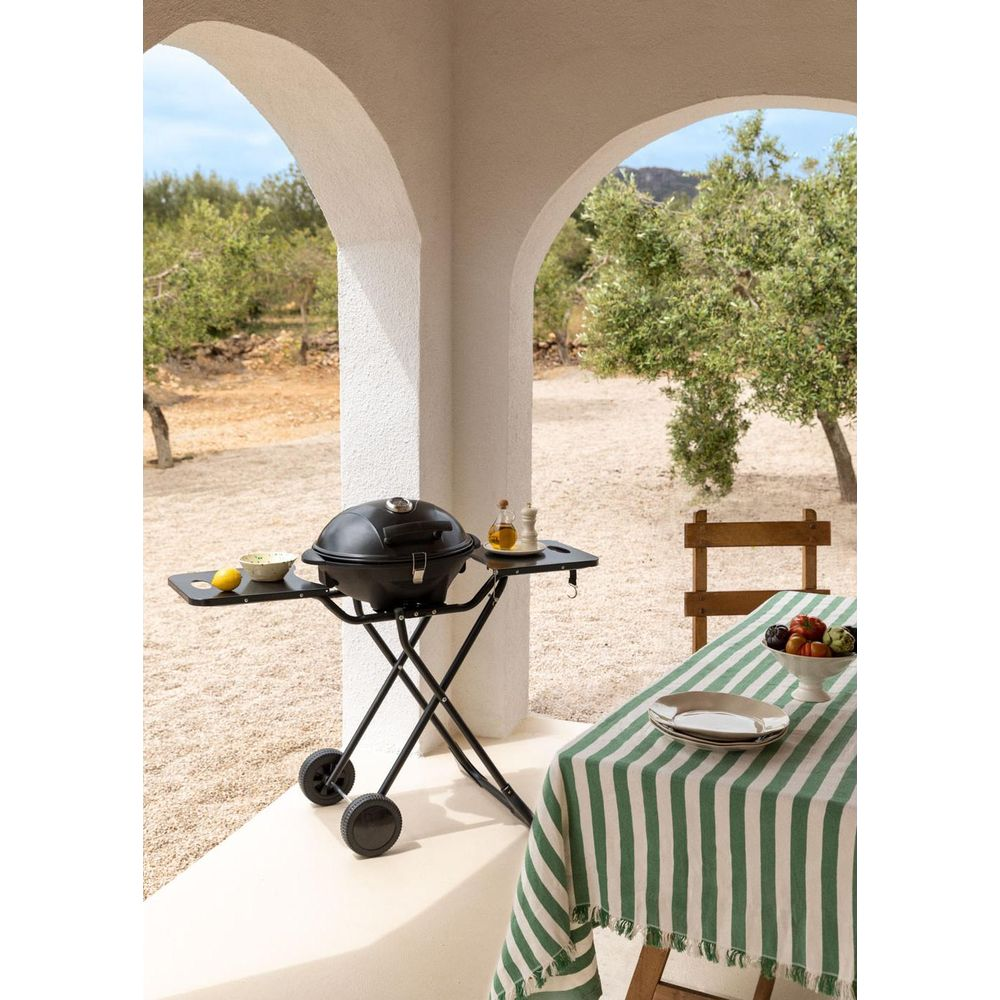 Una parrilla negra en un patio con olivos al fondo.