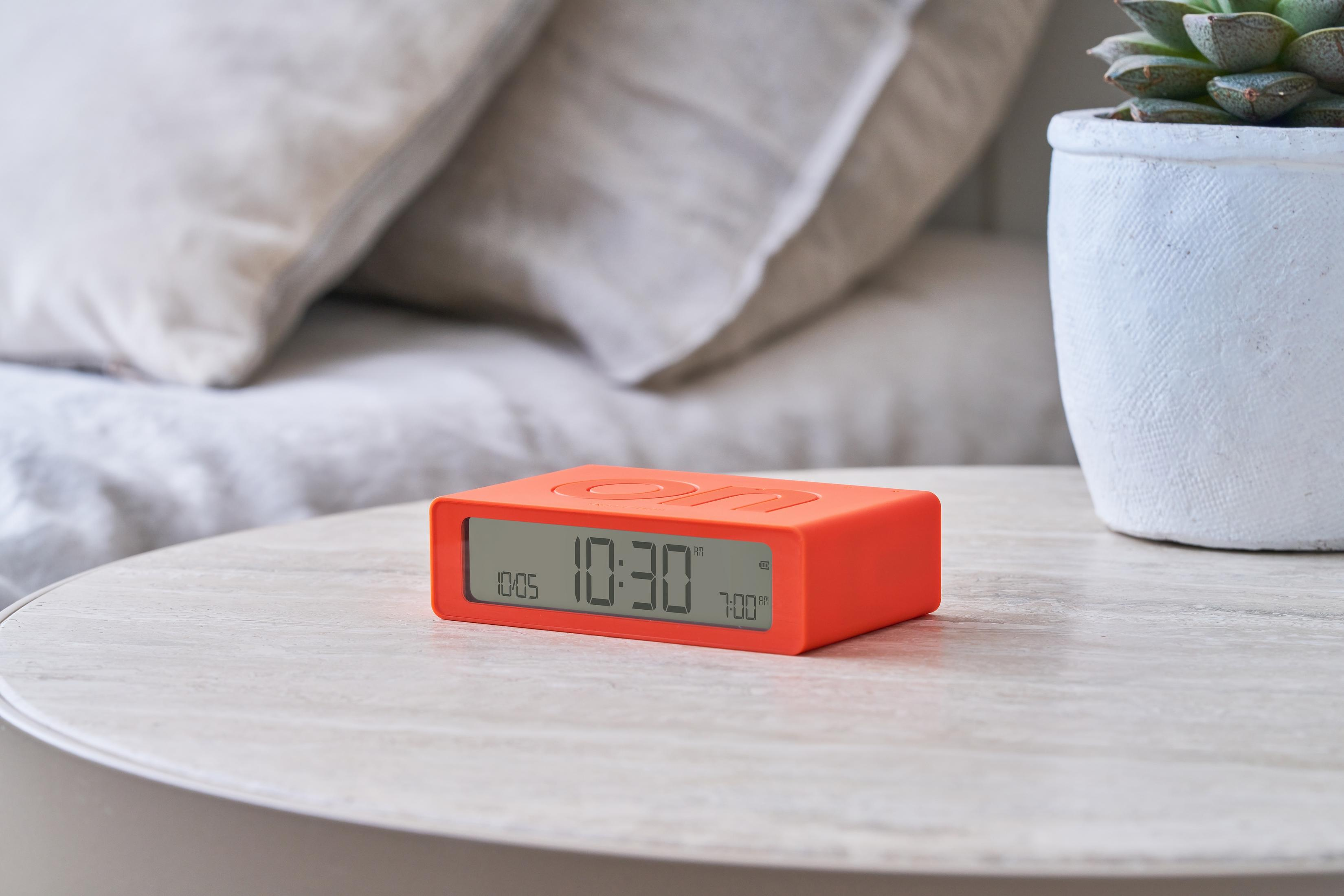 Un réveil numérique orange affiche 10h30 sur une table de chevet près des oreillers.