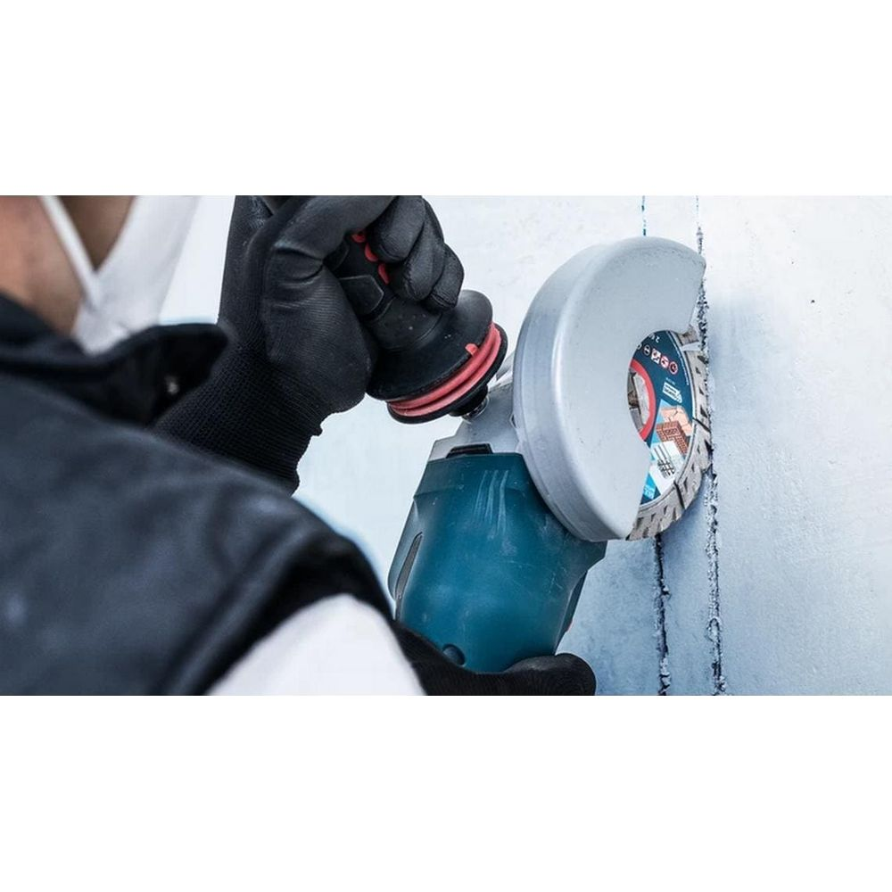 Ein Mann mit Handschuhen benutzt einen Winkelschleifer, um eine Wand zu bearbeiten.