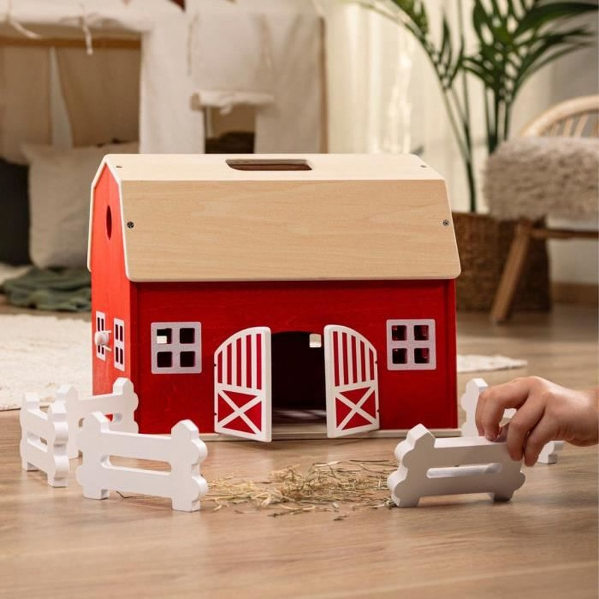 Ein rotes Holzspielzeughaus mit weißem Zaun und einer Hand.