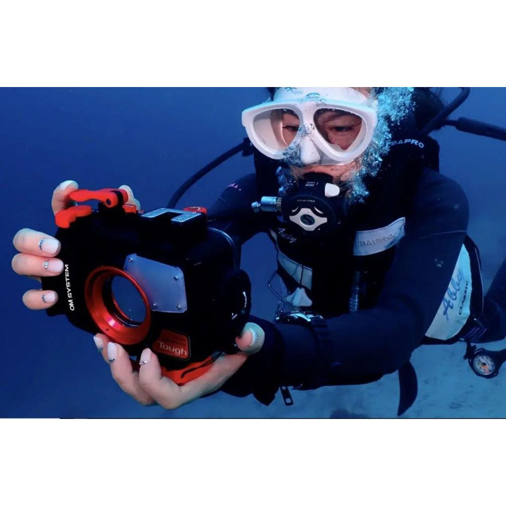 Taucherin mit Kamera im blauen Wasser. Sie trägt einen schwarzen Taucheranzug und weiße Maske.