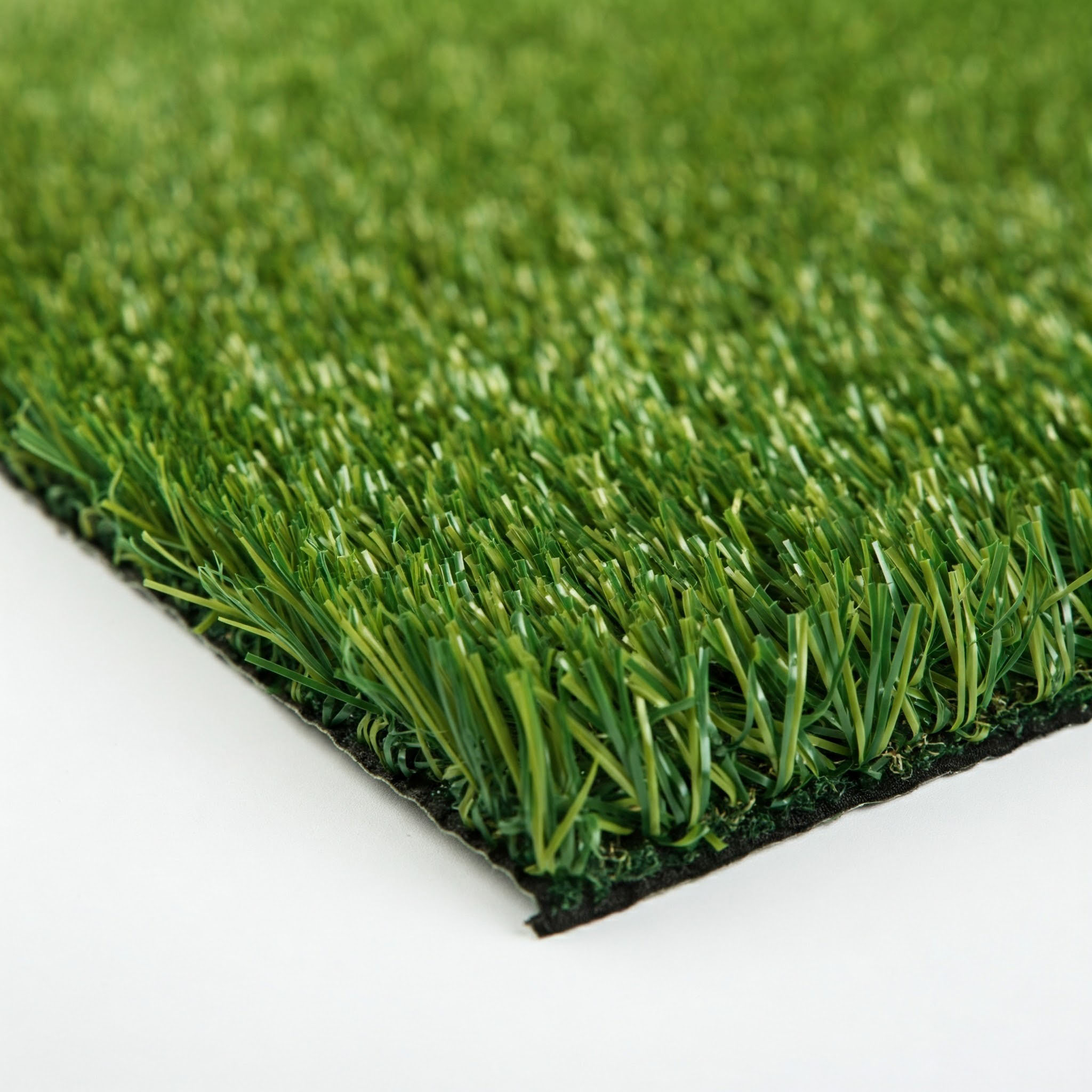 Primer plano de briznas de césped artificial verde sobre fondo blanco. Las briznas son de varios tonos verdes.