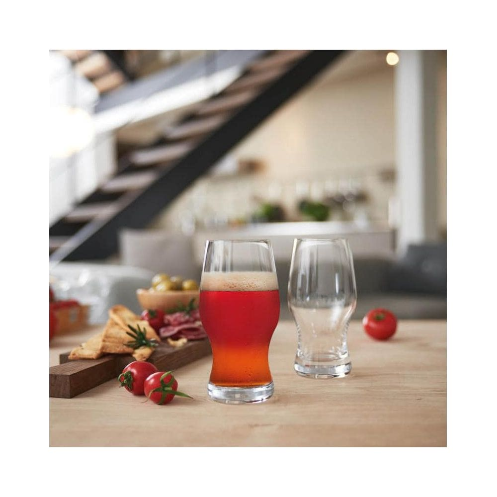 Ein Glas Bier steht neben einem leeren Glas. Ein Snackbrett mit Wurst und Brot ist links.