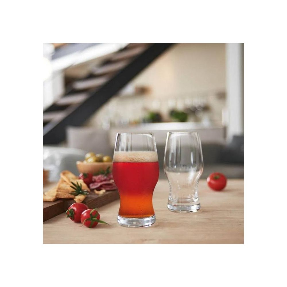 Ein Glas Bier neben einem leeren Glas, garniert mit Tomaten und Oliven.