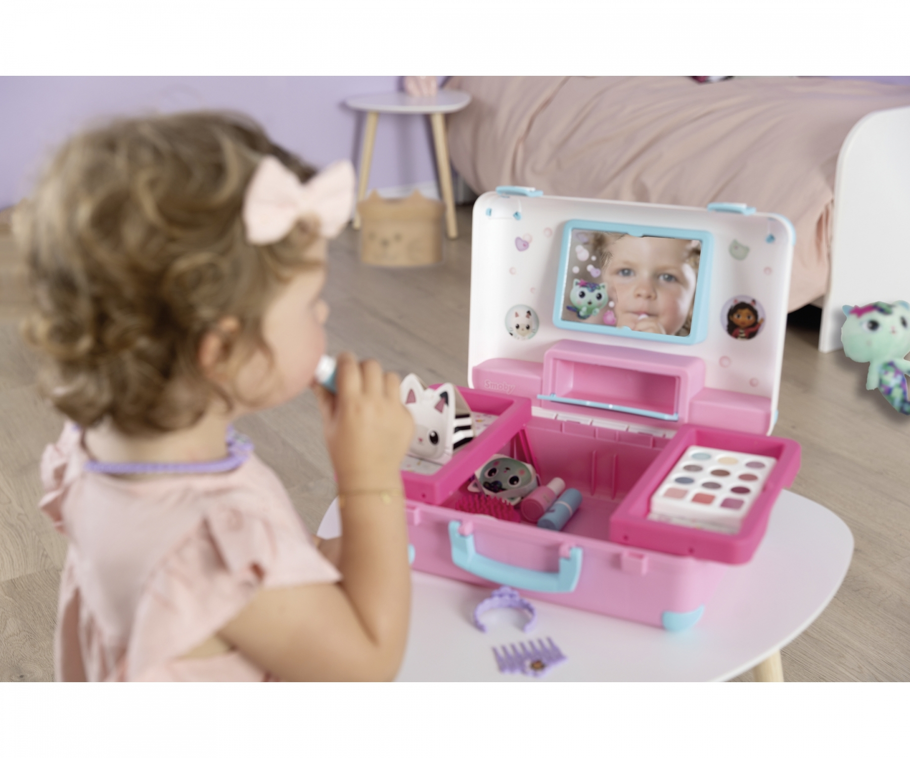 Une petite fille avec un nœud rose dans les cheveux joue avec une trousse de maquillage jouet.