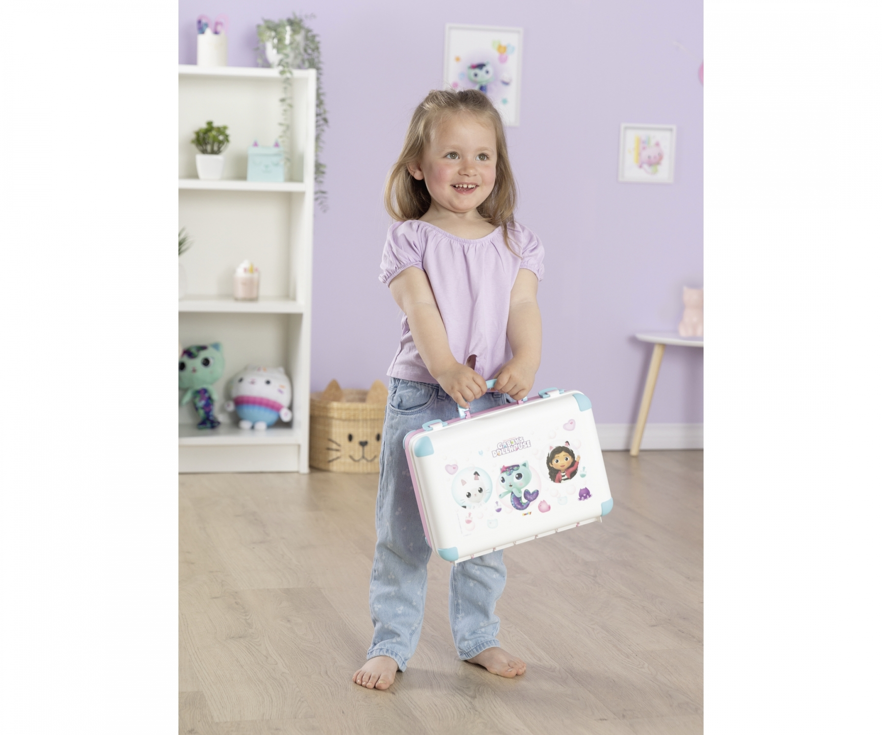 Une jeune fille en jean et chemise violette tient une valise jouet blanche.