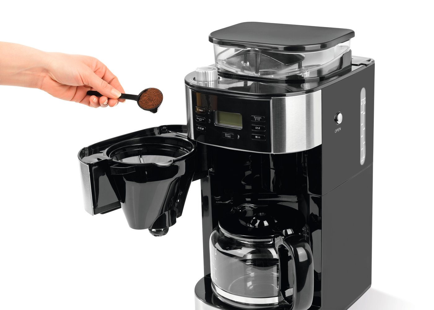 Una mano añade café molido a una cafetera con jarra de cristal.