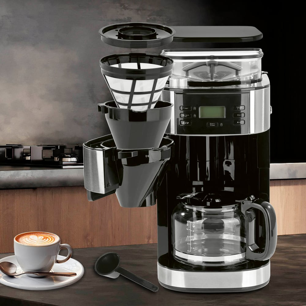 Una cafetera negra con jarra de cristal, filtro de café y una taza de latte art.