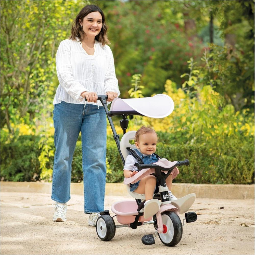Donna spinge bambino in triciclo rosa nel parco.