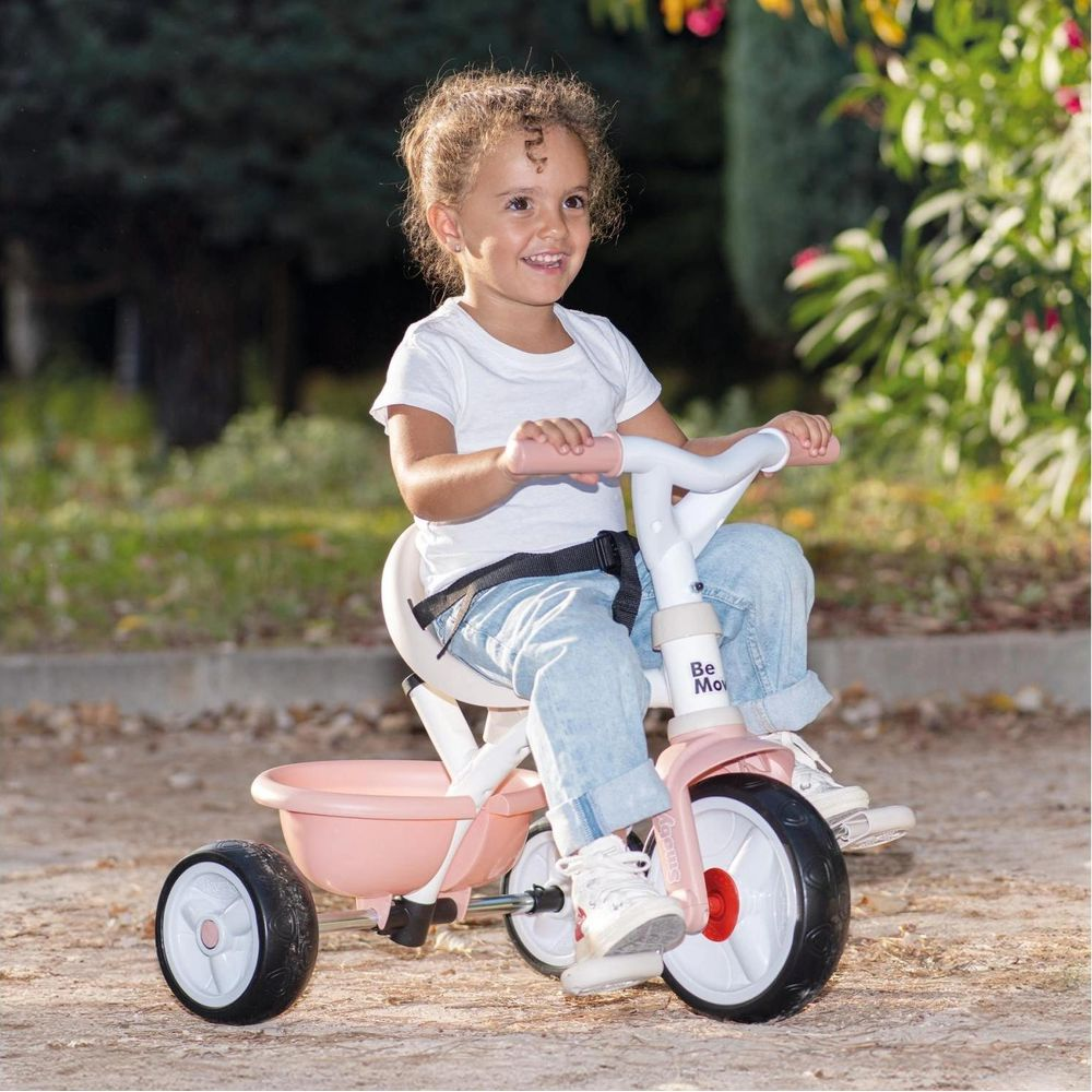 Una bambina guida un triciclo rosa all'aperto, sorridendo.