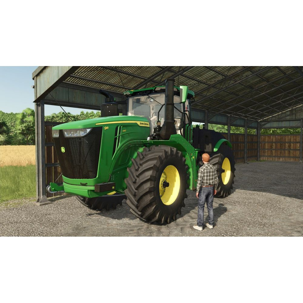 Mężczyzna stoi obok dużego zielonego traktora John Deere w szopie.
