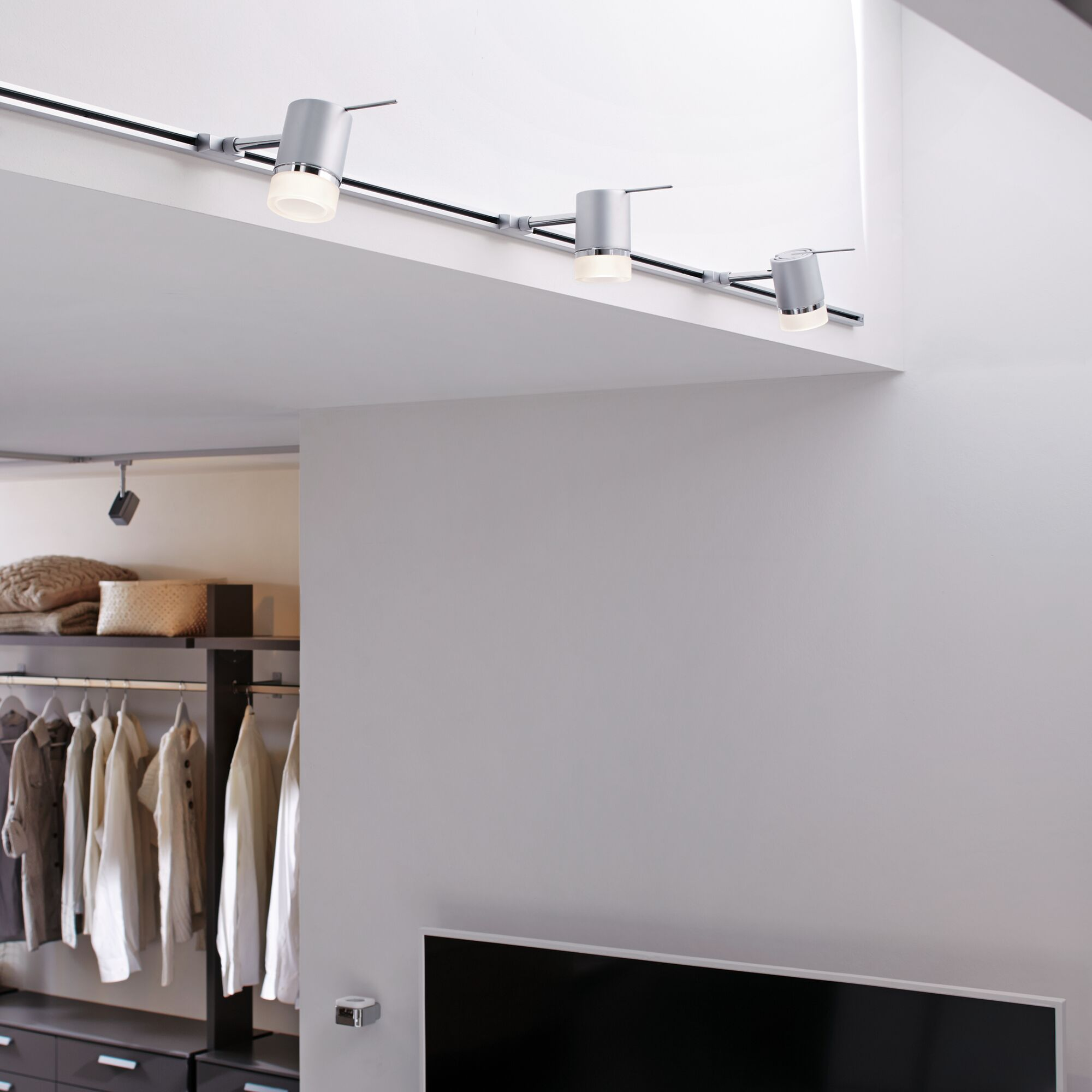 Luci a binario grigie sul soffitto sopra un armadio aperto con vestiti.