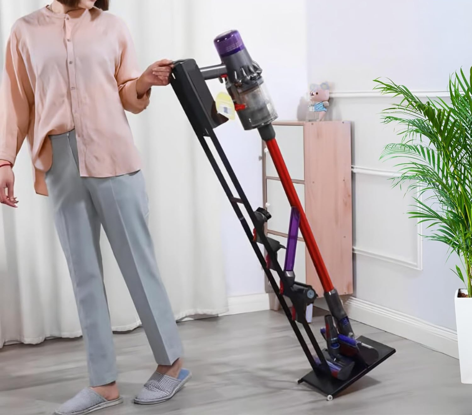 Una persona con camisa rosa y pantalones grises está junto a un soporte para aspiradora.